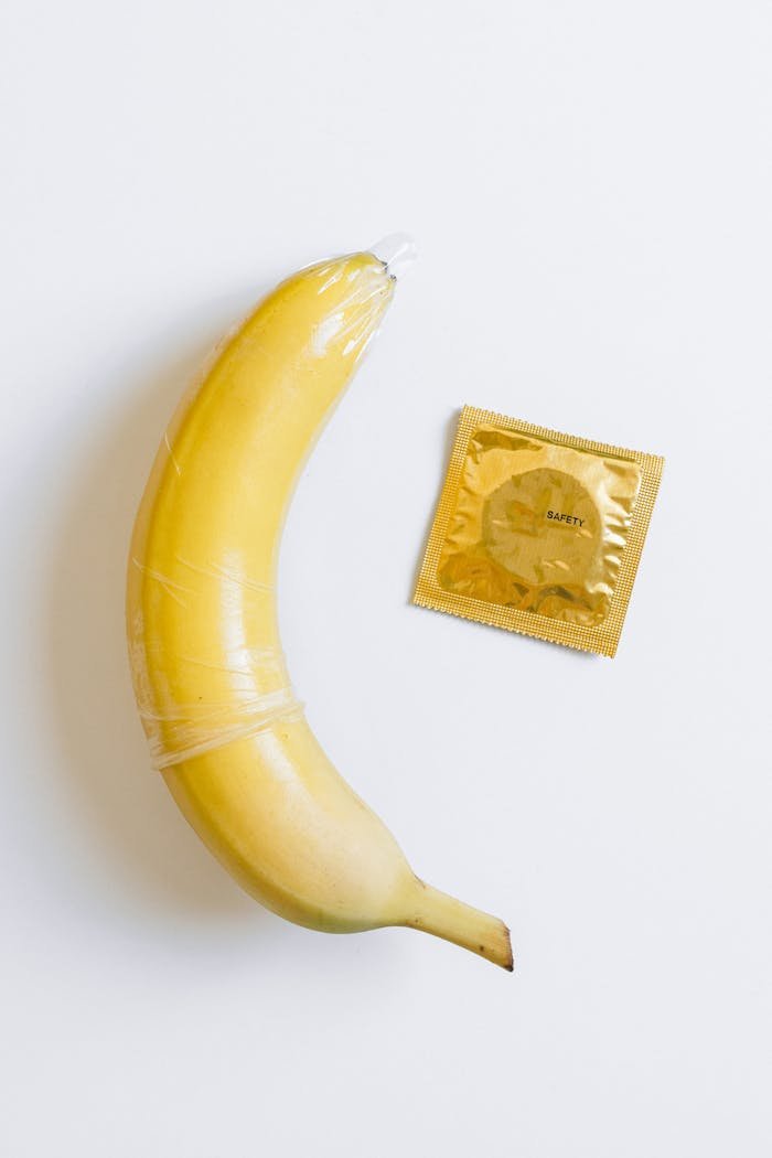 A banana wrapped in a condom next to a packaged condom on a white background, symbolizing safe sex education.